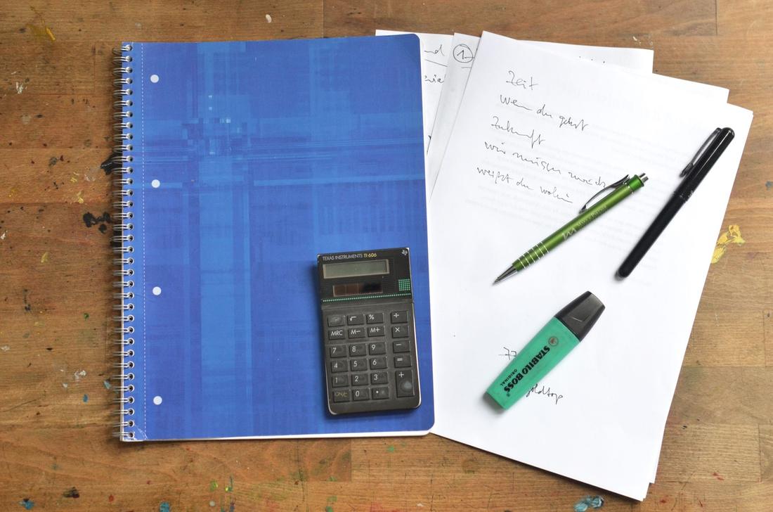 Arbeitsplatz mit Taschenrechner, Notizbuch und Unterlagen auf einem Holzschreibtisch